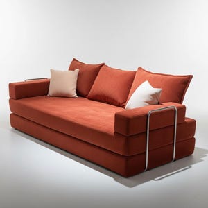 May include: A modern, low-profile sofa in a warm orange hue. It features a rectangular design with a series of stacked cushions and armrests. The sofa includes three back cushions and two smaller accent pillows. Polished metal accents add a touch of elegance.