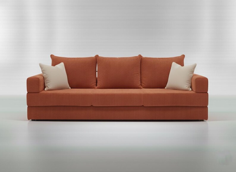 May include: A modern, orange corduroy sofa with three matching back cushions and two off-white accent pillows. The sofa has a low profile and a minimalist design, perfect for a living room or apartment.