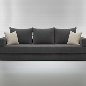 May include: A dark gray, three-cushion sofa with a corduroy texture. Two cream-colored throw pillows are on the ends, and three matching dark gray pillows are against the back. The sofa is a modern design.