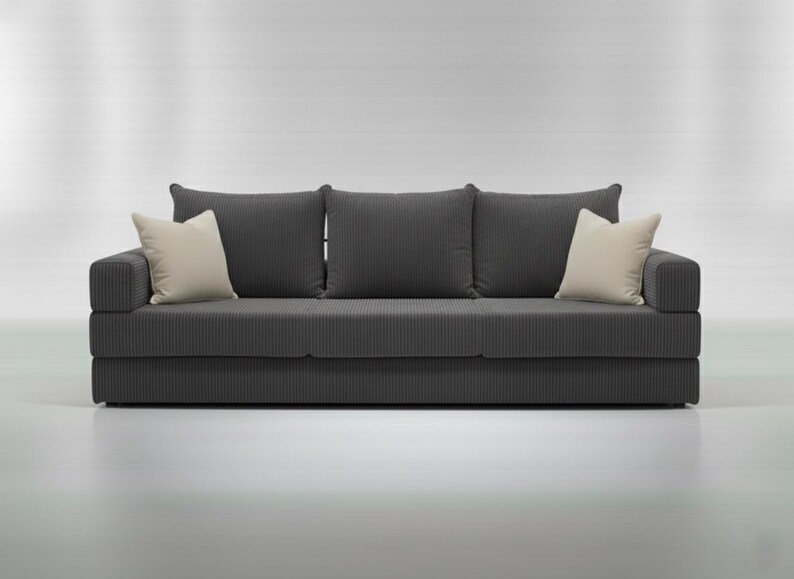 May include: A dark gray, three-cushion sofa with a corduroy texture. Two cream-colored throw pillows are on the ends, and three matching dark gray pillows are against the back. The sofa is a modern design.
