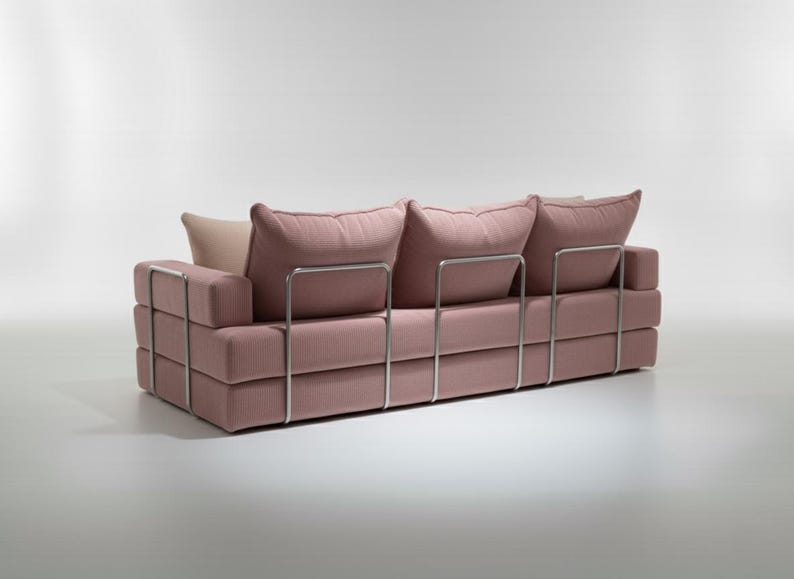 May include: A modern, three-cushion sofa in a soft pink fabric. The sofa features a stacked block design with a stainless steel frame. The cushions are plush and inviting, with a neutral-toned pillow in the back. A stylish piece for any living space.