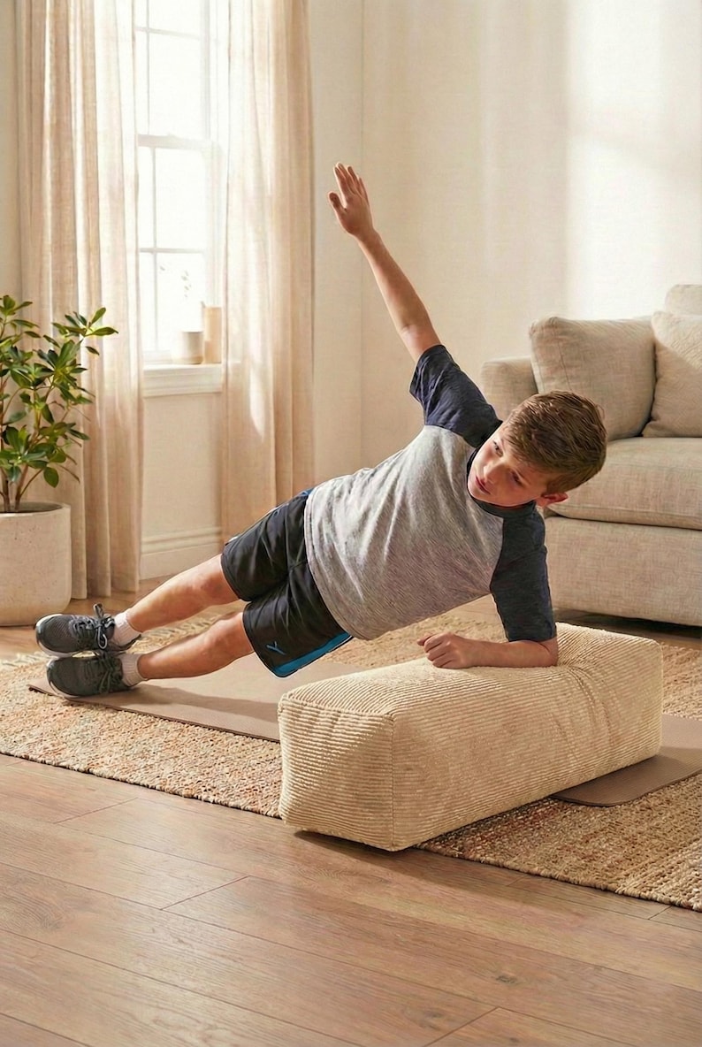 Może przedstawiać: Osoba wykonuje ćwiczenie planku bocznego na beżowym bloku do ćwiczeń sztruksowych. Osoba ma na sobie szarą i granatową koszulkę, czarne szorty i szare trampki. Ćwiczenie wykonywane jest na brązowej macie na tkanej macie.