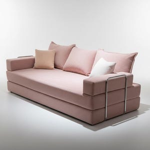 May include: A modern pink sofa with multiple cushions. The sofa has a low profile with a rectangular shape and a metal frame on the armrests. The cushions are in shades of pink and white.