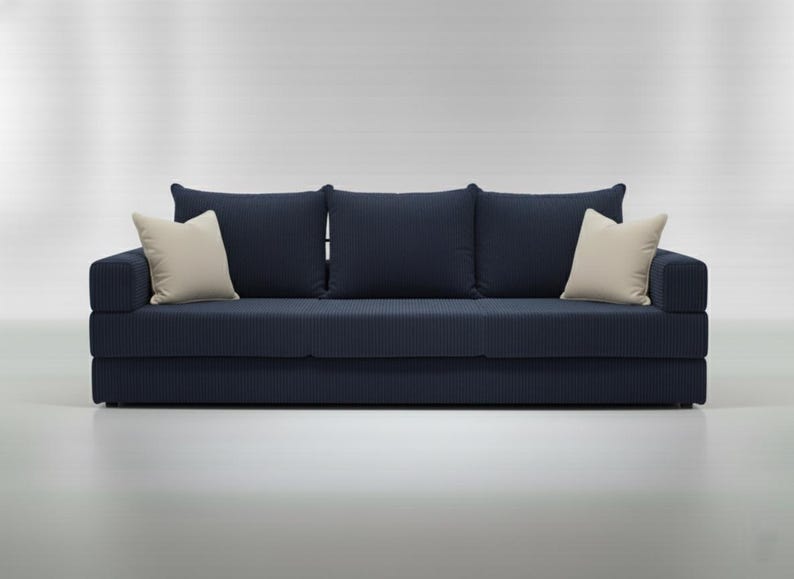 May include: A navy blue sofa with three back cushions and two cream-colored throw pillows. The sofa has a textured, ribbed fabric. The design is modern and minimalist, suitable for a living room or lounge area.