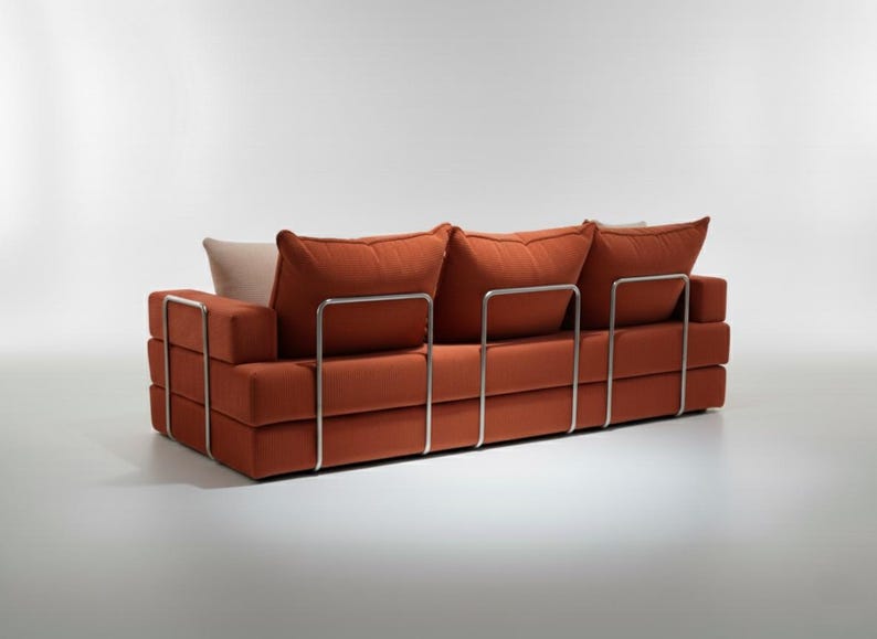 May include: A modern, three-cushion sofa in a burnt orange fabric. The sofa features a rectangular design with a stacked base and back, supported by a polished metal frame. The back cushions are large and plush, with a neutral-colored pillow.