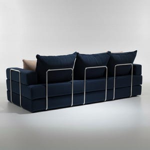 May include: A modern navy blue sofa with a minimalist design. The sofa features a rectangular shape with stacked cushions and a metal frame. It has three large back cushions and two smaller accent pillows.