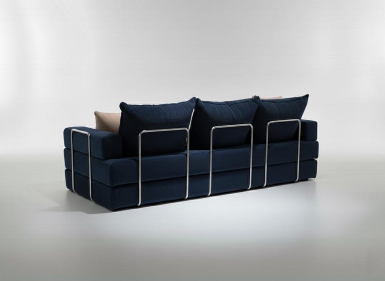 May include: A modern navy blue sofa with a minimalist design. The sofa features a rectangular shape with stacked cushions and a metal frame. It has three large back cushions and two smaller accent pillows.