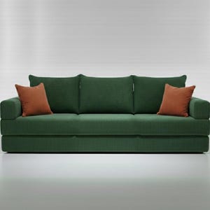 May include: A green corduroy sofa with three back cushions and two rust-colored throw pillows. The sofa has a modern design and is set against a white background. The sofa is approximately 80 inches long.