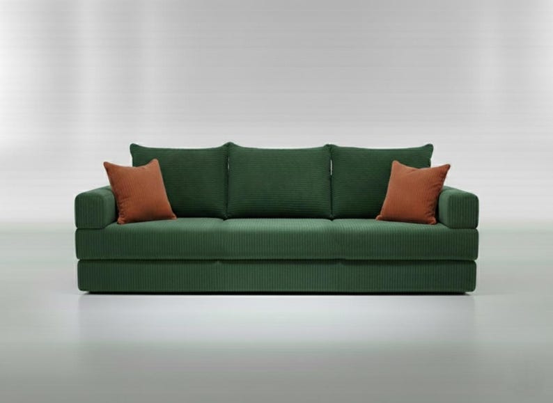 May include: A green corduroy sofa with three back cushions and two rust-colored throw pillows. The sofa has a modern design and is set against a white background. The sofa is approximately 80 inches long.