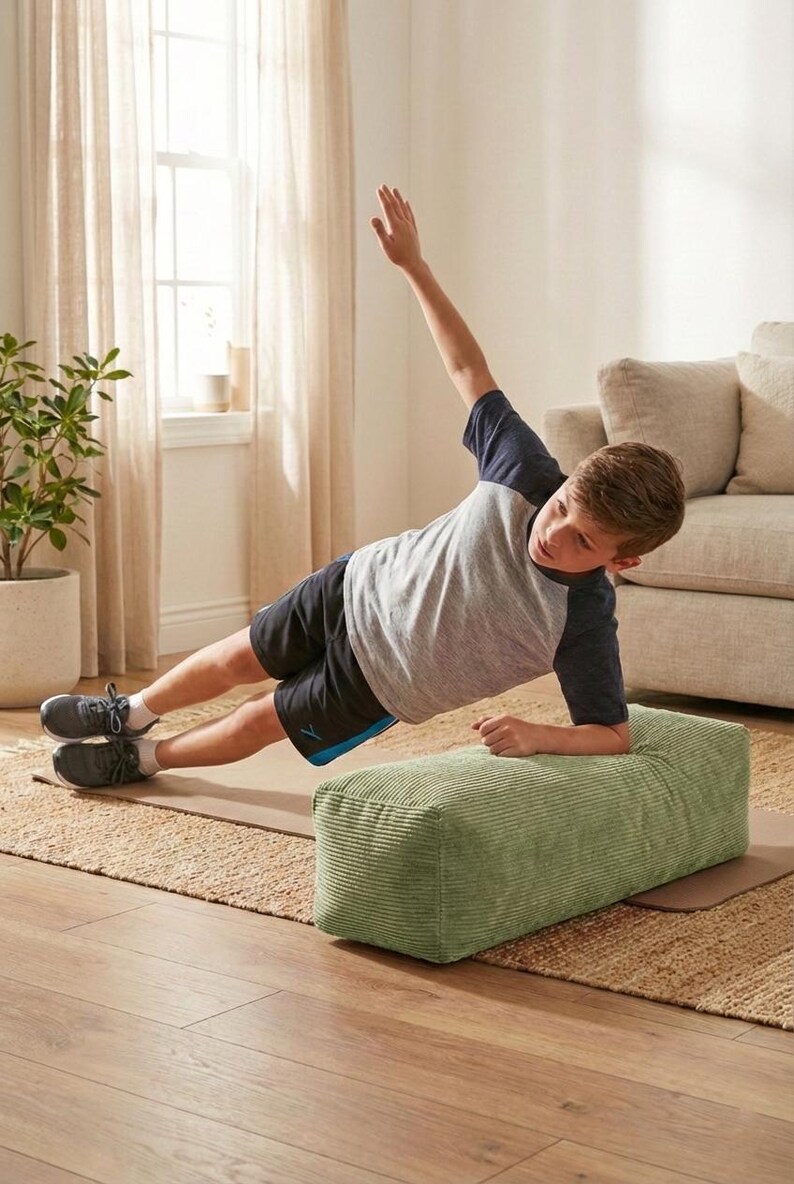 Może przedstawiać: Osoba wykonuje ćwiczenie w pozycji bocznej deski, opierając się na zielonym bloku sztruksowym. Ma na sobie szaro-granatową koszulkę i czarne szorty. Ćwiczenie wykonywane jest na brązowej macie do jogi, z neutralnym tłem.