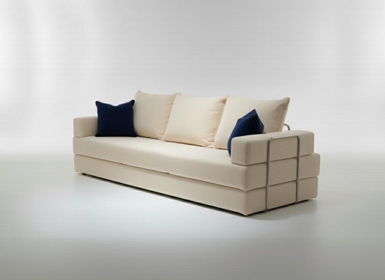 May include: A modern, cream-colored sofa with three off-white cushions and two navy blue accent pillows. The sofa features a geometric armrest design with metal accents, creating a minimalist aesthetic.