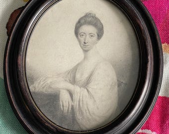Puede incluir: Un retrato ovalado enmarcado de una mujer con un vestido claro. El dibujo en escala de grises está dentro de un marco de madera oscura. La mujer se muestra de pecho para arriba, con los brazos apoyados en una superficie. El fondo presenta un colorido estampado floral.