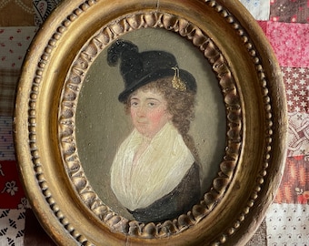 May include: Oval portrait painting of a person wearing a black hat with a gold trim and a white collar. The painting is framed in a gold oval frame.
