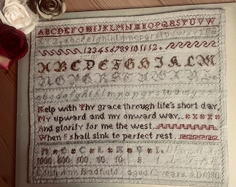 Może przedstawiać: Oprawiony sampler z haftowanymi alfabetami, cyframi i wierszem w czerwonej i brązowej nici. Sampler zawiera tekst "Help with Thy grace through life's short day." Sampler jest datowany na 1080.