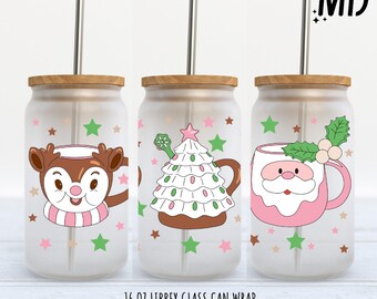 May include: Three frosted glass can wraps with bamboo lids and stainless steel straws. Each features a different Christmas design: a reindeer with a pink scarf, a Christmas tree, and a Santa mug. Pink and green stars decorate the background.