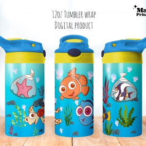 Puede incluir: Tres vasos de 12 oz azules y amarillos con tapa de pajita. Los vasos presentan un tema de Buscando a Nemo con imágenes de Dory, Nemo y una estrella de mar. Los vasos están sobre una superficie de madera.