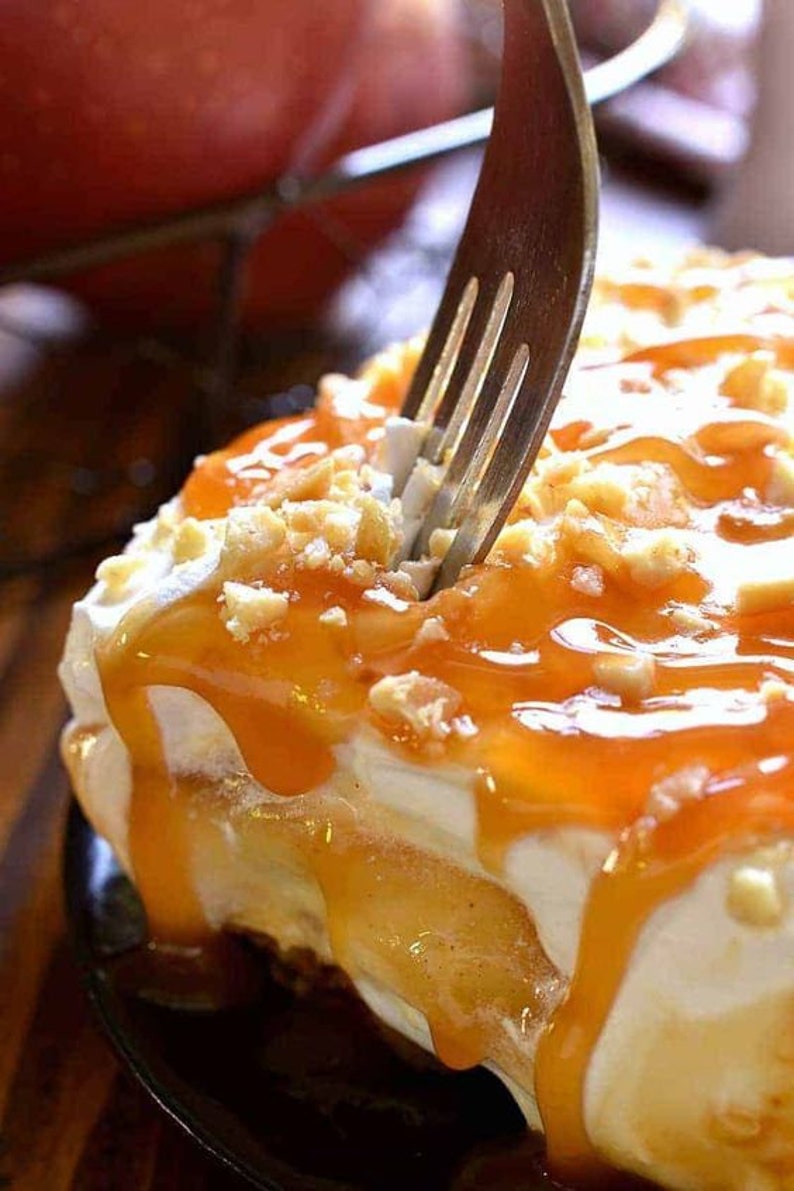 Op de afbeelding: Een vork prikt in een gelaagd dessert met karamelsaus, slagroom en een knapperige topping.