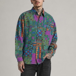 May include: A long-sleeved button-down shirt featuring a vibrant, multi-colored patchwork pattern in shades of green, purple, orange, and blue, paired with charcoal gray denim jeans and black leather shoes, worn with dark-tinted sunglasses.