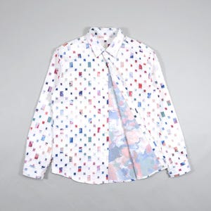 May include: White button-down shirt with a colorful square pattern. The shirt's interior lining features a watercolor-style design. The long-sleeved shirt is unbuttoned, revealing the interior pattern.