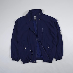 May include: A navy blue jacket with a high collar and a full-length zipper. The jacket has the word "VERSACE" printed vertically on the front and the brand logo on the sleeve. The jacket has a drawstring at the waist and cuffs.
