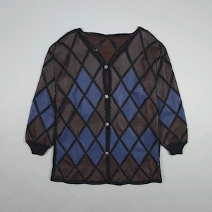 Op de afbeelding: Een vest met lange mouwen en een ruitpatroon. De jas heeft bruine en blauwe ruiten, omrand met zwarte stiksels. De mouwen eindigen in zwarte manchetten. De knopen zijn zilverkleurig. Het kledingstuk wordt gepresenteerd op een lichtgrijze achtergrond.
