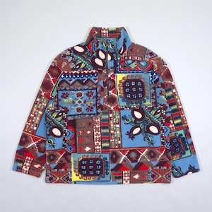 Puede incluir: Un jersey de forro polar de manga larga con cuello alto y cierre de cremallera de un cuarto. El colorido diseño de patchwork presenta patrones geométricos y florales en tonos azules, marrones, rojos y amarillos. El forro polar es suave y cálido.