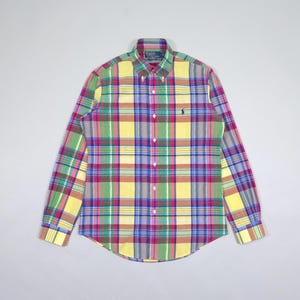 May include: A long-sleeved, button-down shirt in a vibrant plaid pattern. The shirt features a mix of colors including yellow, green, pink, blue, and purple. A small logo is visible on the chest. The shirt is made of a lightweight fabric.