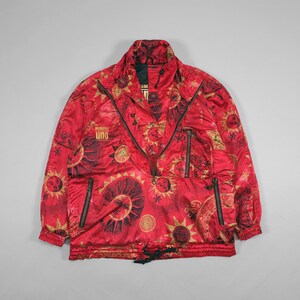 May include: Red vintage anorak with a sun and star pattern. The jacket has a half-zip closure, two side pockets, and the text "NUMERU UNO". The anorak has a drawstring at the waist and black zippers.