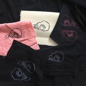 Könnte beinhalten: Fünf Stoffquadrate mit unterschiedlichen Hintergrundfarben und schwarzen Tinten-Schädelmotiven. Die Stoffquadrate sind zu einem Stapel angeordnet.