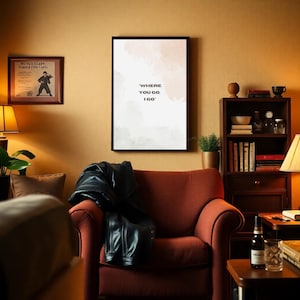 Könnte beinhalten: Ein gemütliches Wohnzimmer mit einem roten Sessel, einer schwarzen Lederjacke und einem gerahmten Druck mit dem Text "WHERE YOU GO, I GO". Ein Bücherregal aus Holz und ein kleiner Beistelltisch mit einer Flasche und Gläsern sind ebenfalls zu sehen.