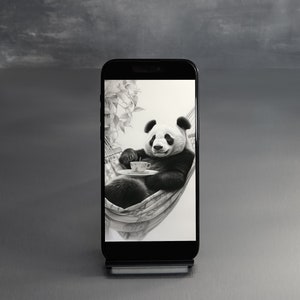 May include: A black and white panda bear relaxing in a hammock with a cup of tea. The panda is sitting in a hammock with a white background. The image is on a smartphone screen.