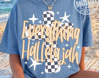 May include: A blue short-sleeve t-shirt featuring a large black and white checkered cross graphic. The text Everything Hallelujah is printed in a light orange script font over the cross, surrounded by white star shapes and a butterfly necklace.