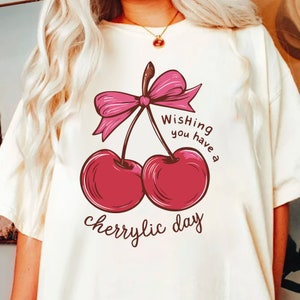 Może przedstawiać: Biała koszulka z nadrukiem r&oacute;żowej wiśni i tekstem "Wishing you have a cherrylic day".