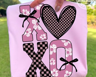 Puede incluir: Una sudadera rosa claro con las letras "XO" y un diseño de corazón. Las letras "XO" están decoradas con un estampado floral y un estampado de tablero de ajedrez en blanco y negro. El corazón es a cuadros en blanco y negro.