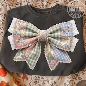 May include: Dark gray sweatshirt featuring a large, decorative bow. The bow is made of patchwork fabric in pink, green, and blue floral and gingham patterns, trimmed with white lace and faux pearls. Two butterfly appliqués add detail. The design is from Digitaira Design.