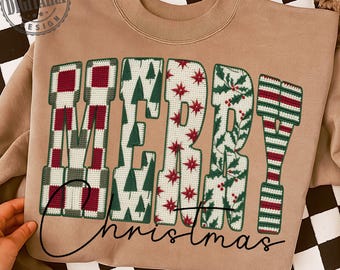 Può includere: Una felpa beige con la scritta "MERRY Christmas". Le lettere sono decorate con motivi festivi in rosso, verde e bianco, tra cui alberi di Natale, stelle e foglie di agrifoglio. Il testo è in un carattere corsivo.