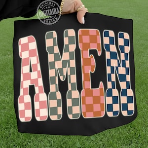 May include: Black tote bag with the word "AMEN" in large, retro-style letters. The letters are filled with a checkered pattern in shades of pink, green, orange, and blue. The bag is held against a background of green grass.