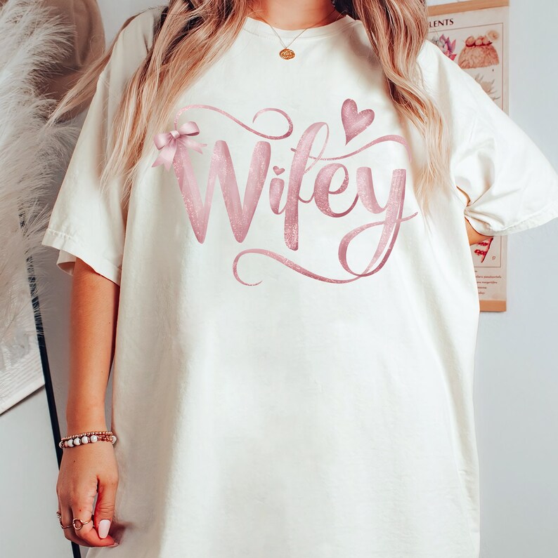May include: White oversized t-shirt with a pink glitter design that says "Wifey" with a pink bow and heart.