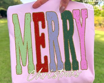 Può includere: Una felpa rosa chiaro con la scritta "MERRY CHRISTMAS" a lettere grandi e colorate. La parola "MERRY" è in verde, rosso, viola e rosa, con contorni dorati. La parola "Christmas" è in corsivo.
