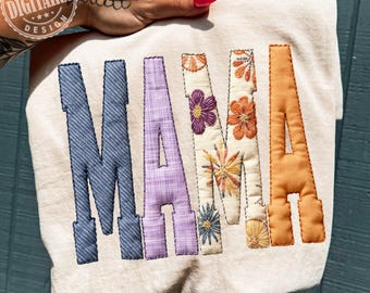 以下が含まれることがあります： クリーム色のスウェットシャツ。大きくカラフルな刺繍文字で「MAMA」と書かれています。「M」は青いデニム、「A」はラベンダーのチェック柄、2つ目の「M」は花柄、最後の「A」はオレンジ色です。