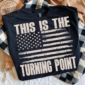 May include: Black t-shirt with a distressed American flag design. The shirt features the text "THIS IS THE TURNING POINT" in a bold, white font, with the flag's stars and stripes incorporated into the design.