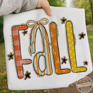 May include: White fabric with the word "FALL" embroidered in autumn colors. The letters are decorated with plaid, stripes, and polka dots, and surrounded by star accents. The design has a stitched border and a bow.