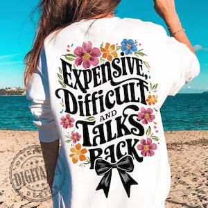 May include: White t-shirt with a floral design and the text "Expensive, Difficult and Talks Back" in black lettering. A black bow is centered below the text.