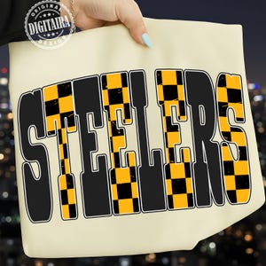 Op de afbeelding: Crèmekleurige draagtas met het woord "STEELERS" in grote, vette letters. De letters zijn zwart met geel en zwart geblokte accenten. De tas wordt door een hand omhoog gehouden.