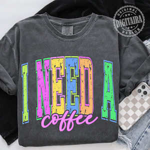 May include: Dark gray long-sleeve shirt with the text "I NEED A coffee" in a colorful, distressed font. The text features neon green, pink, yellow, blue, and orange colors. The shirt has a vintage, worn look.