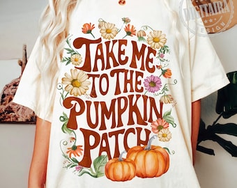 Peut inclure: T-shirt blanc avec un motif brun qui dit "Take Me To The Pumpkin Patch". Le motif est entouré de fleurs colorées et de deux citrouilles orange.