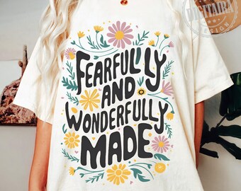 Op de afbeelding: Een wit T-shirt met een bloemenprint en de tekst "Fearfully and Wonderfully Made" in zwarte letters.