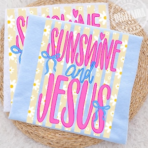 Op de afbeelding: Twee lichtblauwe en witte decoratieve handdoeken met de woorden "Sunshine and Jesus" in roze script. De handdoeken hebben een geel en wit gestreepte achtergrond met madeliefjes- en hartaccenten en blauwe strikdetails.