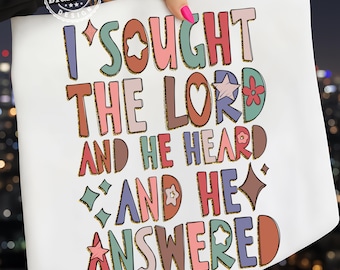 May include: White tote bag with the text "I Sought The Lord And He Heard And He Answered" in colorful, retro-style lettering. The design includes stars, hearts, and floral elements with gold glitter accents.