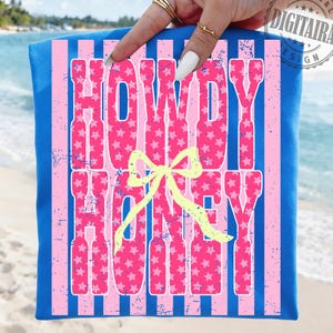 May include: A blue beach towel with pink vertical stripes and the words "HOWDY HONEY" in pink letters filled with white stars. A yellow bow is centered below the text. The towel is held up by a hand with rings on the fingers.